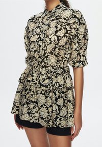 Blusa nera a fiori con maniche corte, vita arricciata e tessuto testurizzato. Presenta motivi floreali color crema e un colletto con bottoni.