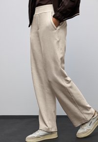Pantalons larges beige en tissu doux avec une finition texturée, dotés de poches latérales et d'une taille élastique.