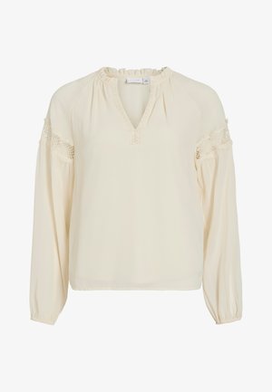 Blusa color crema con scollatura a V, collo arricciato, maniche lunghe e dettagli in pizzo sulle spalle. Realizzata in tessuto leggero e morbido.