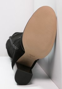 Svart mocka ankelboot med en slät, rund tå och en fyrkantig klack. Sula i beige med ett prydligt mönster för grepp och prägling.