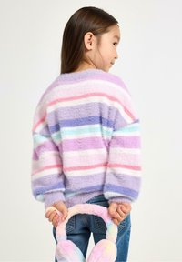 Flauschiger, mehrfarbiger gestreifter Pullover in Lavendel, Pink und Blau. Das Kind hält pastellfarbene Ohrenwärmer und trägt blaujeans mit einem abgerundeten Schnitt.