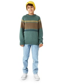 Stickad tröja i teal med gula, bruna och blå horisontella ränder; rund hals, nedhasade axlar, matchad med ljusblå jeans och vita sneakers.