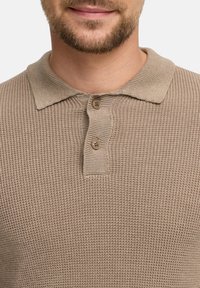 Polo shirt a maglia beige con un tessuto testurizzato, caratterizzato da un colletto classico e due bottoni marroni sul collo.