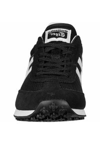 Svart sportskor med ovandel i mesh och mocka, vita detaljer, runda snören och sula av texturerat gummi med ett mönster av små nitar.