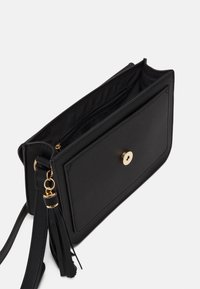 Borsa in ecopelle nera con forma piatta, dotata di una pattina frontale, accessori in oro, tasca interna con zip e un dettaglio con frangia sulla tracolla.