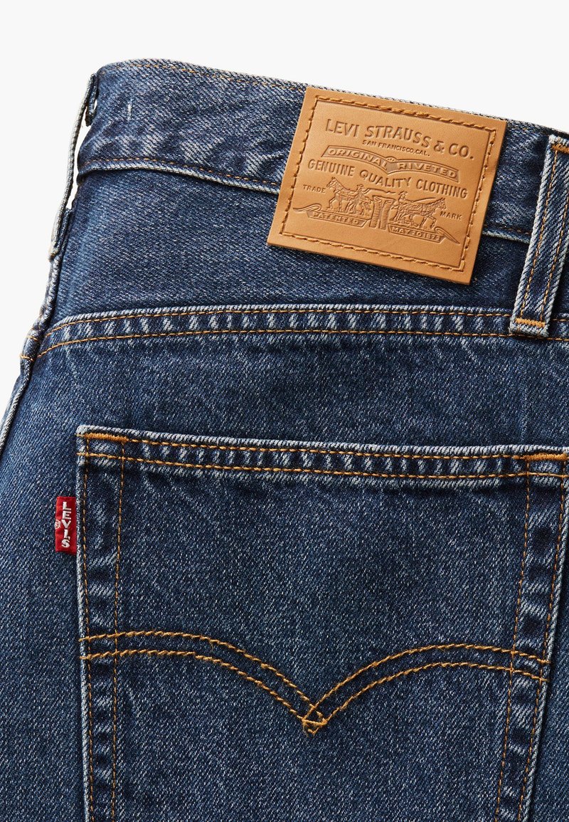 Blå denimjeans med orange sömmar, med en brun läderetikett präglad med "Levi Strauss & Co." och en röd Levi's-flik på bakfickan.