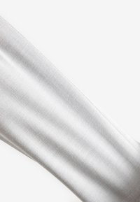 Gros plan sur une manche en tissu blanc texturé avec des coutures visibles le long du bord, présentée sur un fond blanc uni.