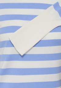 Haut en tricot rayé avec des rayures horizontales bleu clair et blanches. Comprend un accent texturé à manches côtelées blanches. Tissu doux avec une finition lisse.