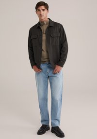 Jachetă button-up de culoare gri închis, cu două buzunare pe piept, purtată peste un top bej, asortată cu blugi bleu deschis și pantofi negri cu șireturi.