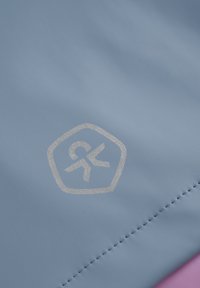 Ljusblått tyg med en slät textur har en silverfärgad hexagonal logo. Kanten är sydd och övergår till en rosa detalj.