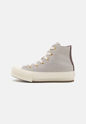 Baskets montantes gris clair avec lacets blancs, œillets dorés, semelle blanche en caoutchouc texturée et languette de talon foncée vues de côté.