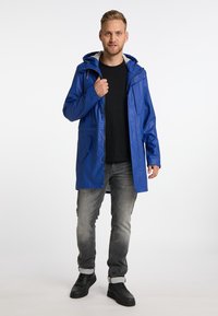 Blå vattentät jacka med huva, dragkedja och tryckknappar, framfickor och en slät yta, i kombination med grå jeans och svarta skor.