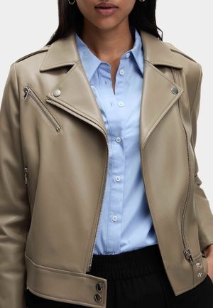 Beżowa kurtka motocyklowa z eko skóry z asymetrycznym zamkiem błyskawicznym, zatrzaskami i zapinanymi na zamek kieszeniami, zestawiona z jasnoniebieską koszulą na guziki.