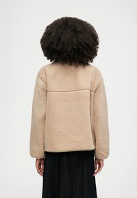 Beige sherpa fleece pullover with a rounded neckline, dropped shoulders, and wide sleeves. Features a flat seam design on the back.