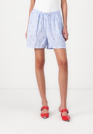 Personne portant un short bleu clair avec un petit imprimé floral rouge et un cordon de serrage, associé à des chaussures à talons rouges à bout pointu avec des boucles.