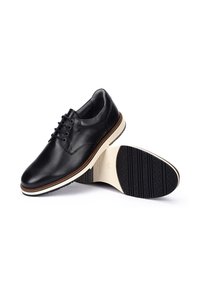 Zapatos de cuero negro con punta redonda, diseño con cordones, suela blanca y marrón, y suela exterior de goma negra texturizada. Notables acentos de costura.