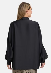 Blusa nera in satin con maniche lunghe e voluminose, colletto classico e dettagli con bottoni ai polsini, caratterizzata da una texture liscia e morbida.