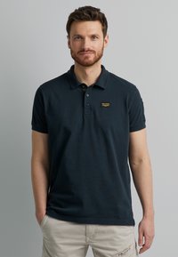 Navyblaues Poloshirt aus weichem Stoff mit einer Knopfleiste mit drei Knöpfen, kurzen Ärmeln und einem kleinen Logopatch auf der Brust.