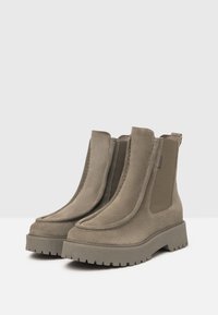 Suede ankle boots in light brown with elastic side panels, chunky rubber soles, and a rounded toe design. Textured finish throughout.