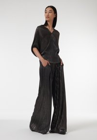 Metallisch zwarte outfit met een losse, oversized top en wijde, gestreepte broek, met ribbelstructuur en subtiele glans.