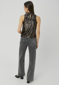 Débardeur noir en sequins avec le dos en découpe, associé à un jean gris à jambes larges et des talons noirs. Présente un aspect brillant et texturé.