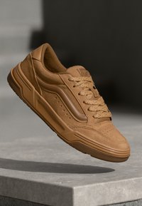 Sneaker in suede beige con tomaia testurizzata, chiusura con lacci, dettagli perforati, suola in gomma e accenti marroni a contrasto sui lati.