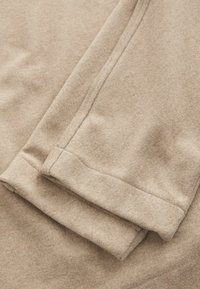 Beżowy polar złożony, z widocznymi szwami wzdłuż krawędzi, charakteryzujący się miękką fakturą i gładkim wykończeniem.