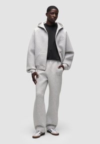 Felpa con cappuccio grigia chiara, dotata di tasca frontale, abbinata a pantaloni della tuta coordinati. Tessuto morbido, vestibilità rilassata e dettagli del logo sottili.