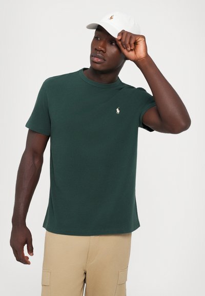 T-shirt en coton vert avec un col rond et des manches courtes, arborant un petit logo brodé en or contrasté sur la poitrine gauche.