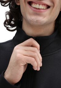 Giacca nera con zip e colletto alto, caratterizzata da una texture liscia. Una mano sta aggiustando la zip vicino al mento.