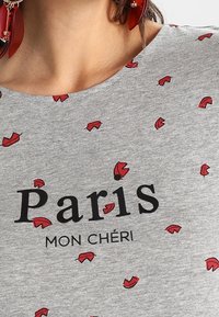 Šedé tričko s potiskem "Paris MON CHÉRI" v černé barvě, doplněné rozptýlenými červenými vzory listů. Měkká tkanina a kulatý výstřih.
