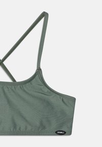 Grønn bikini topp med tynne, kryssende stropper. Laget av glatt stoff, med et logo merke på siden for merkeidentifikasjon.