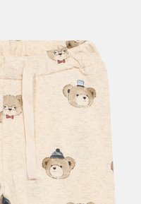 Μπεζ παντελάκια για μωρά με εκτυπωμένα πρόσωπα αρκούδας που φοράνε γυαλιά, παπιγιόν, καπέλα υψηλής ραπτικής και χειμερινά καπέλα, καθώς και λευκή κορδόνι στη μέση.