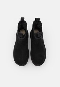 Botas de tobillo de ante negro con forro suave, paneles laterales elásticos y tiradores. Punta redondeada y suela de goma plana para mayor comodidad.