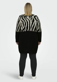 Zwart en crèmekleurige gebreide cardigan met een zebrapatroon op de bovenhelft, een volledig zwarte onderzijde en lange mouwen.
