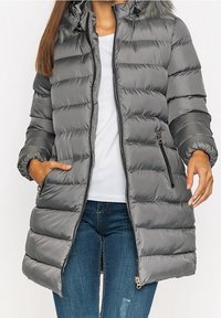 Šedá péřová bunda s kapucí, předním zipem, elastickými manžetami a bočními kapsami. Materiál je lesklý a prošívaný s jemným kožíškovým lemováním.