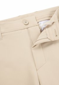 Pantaloni beige con una texture liscia, dotati di chiusura con bottone, patta con zip e passanti per cintura. Design pulito con dettagli di cucitura discreti.