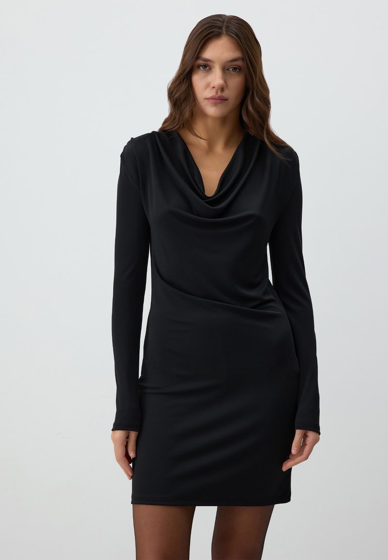Zwarte langesleeve jurk met een gecolladeerde halslijn, gemaakt van gladde stof. Strakke pasvorm, tot halverwege de dij, met subtiele drapering en geen zichtbare patronen.