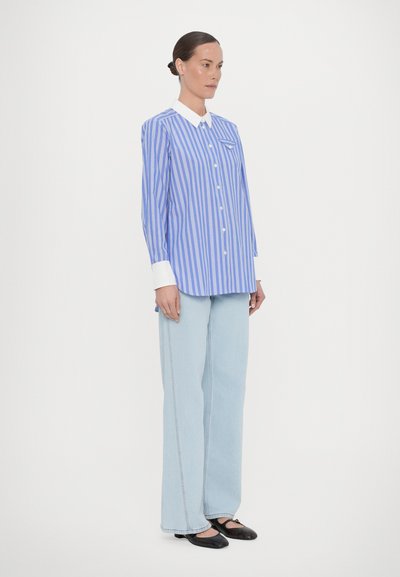 Blue and white striped long-sleeve shirt with a button closure, featuring a white collar and a chest pocket, paired with light blue wide-leg jeans.