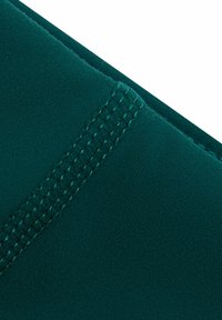 Zbliżenie na ciemnozielony materiał z widocznym podwójnym szwem biegnącym diagonalnie wzdłuż rogu.