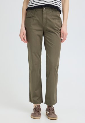 Person iført olivengrønne bukser med lige ben, en sort-hvid stribet cropped top, og brune sneakers med hvide striber.