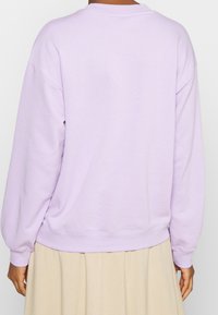 Sudadera lavanda con puños y dobladillo acanalados, que presenta un corte holgado y una textura suave. La vista trasera muestra un diseño simple y minimalista.