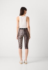 Tijgerprint leggings van rekbaar materiaal, tot aan de knie, met een zwarte tailleband met logo-tekst. Gepaard met een witte tanktop.