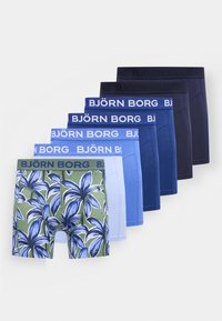 Six paires de caleçons pour hommes dans un dégradé de nuances de bleu, avec une paire verte ornée d'un grand motif floral bleu, toutes munies de ceintures Björn Borg.