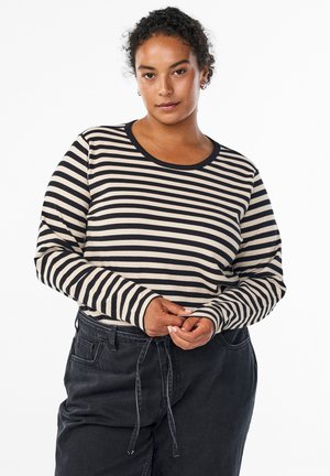 Randig långärmad topp i beige och svart, ribbat material, rund halsringning, med svarta manschetter. Buren med mörka högmidjade byxor.