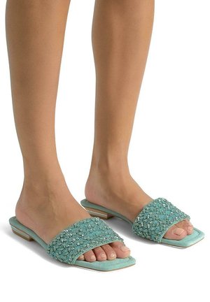 Sandalias planas en color azul verdoso con una amplia correa decorada con strass, suela plana y un acabado de ante texturizado.