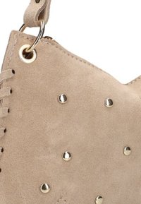 Beige suède tas met een gestructureerd oppervlak, voorzien van goudkleurige studs en eyelets langs de bovenrand.