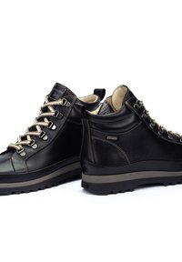 Bottes de randonnée en cuir noir avec des lacets beige, doublure texturée, col rembourré et semelles en caoutchouc robustes. Présente un logo sur la languette et sur le côté.