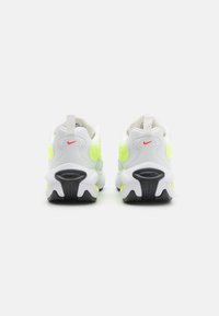 White and neon yellow athletic shoes with a textured upper, thick sole, and distinctive black accents. Features a pull tab on the heel.