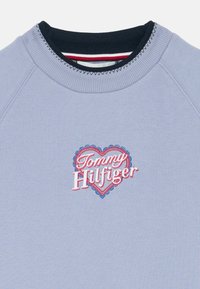 Γαλάζια φόρμα με ναυτικό γιακά και κεντημένο λογότυπο καρδιάς που γράφει "Tommy Hilfiger" σε κόκκινη, λευκή και μπλε κλωστή.